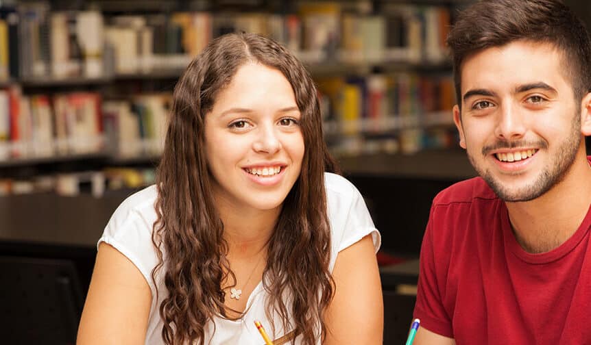 Photo of two students, a young woman on the left and a young man on the right, in front of a bookshelf filled with books.