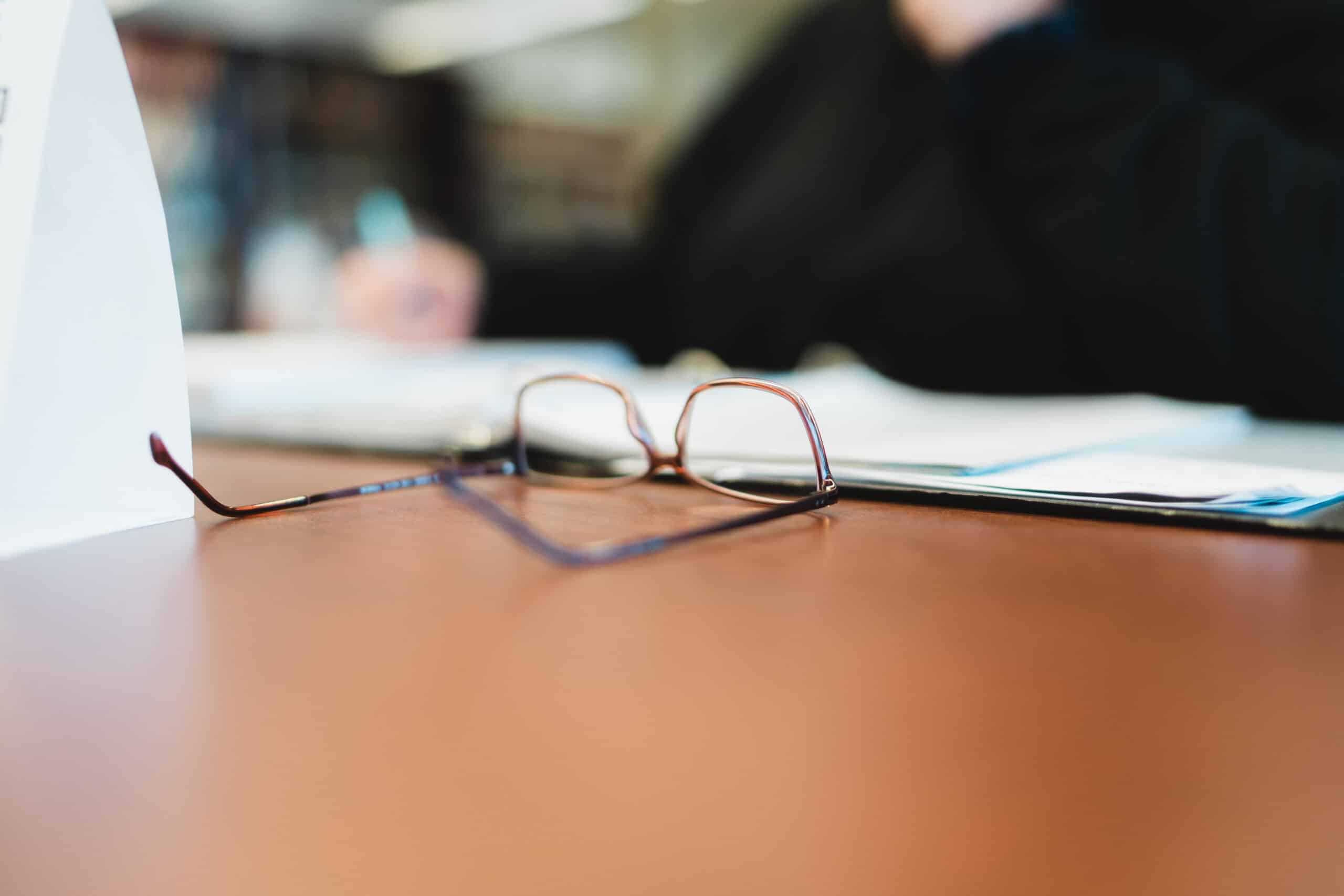 Photo of a desk with papers and eyeglasses on the desk.