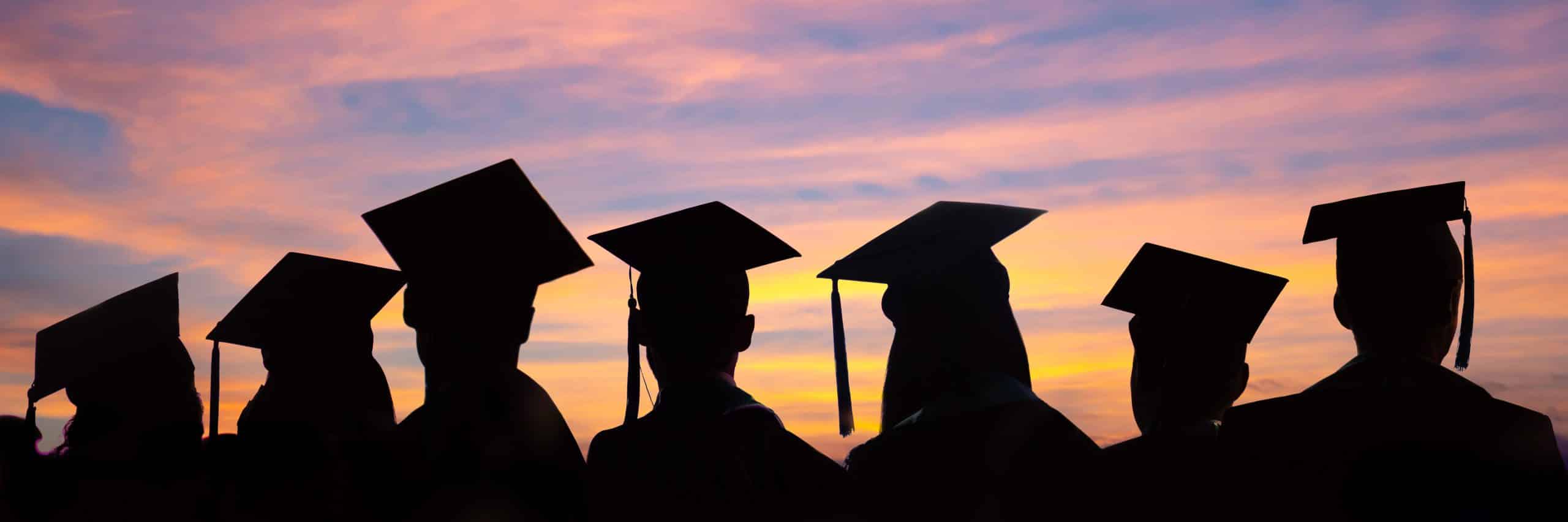 Image of a colorful sky with silhouettes of graduates in the foreground.