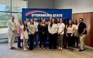 A group of student leaders and staff members pose together in front of a DSCC backdrop, smiling during the President’s Student Leadership Academy graduation ceremony.