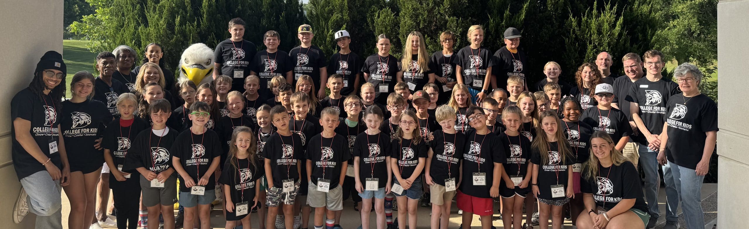 Large group of students standing outside posing with the eagle mascot during the College for Kids event.