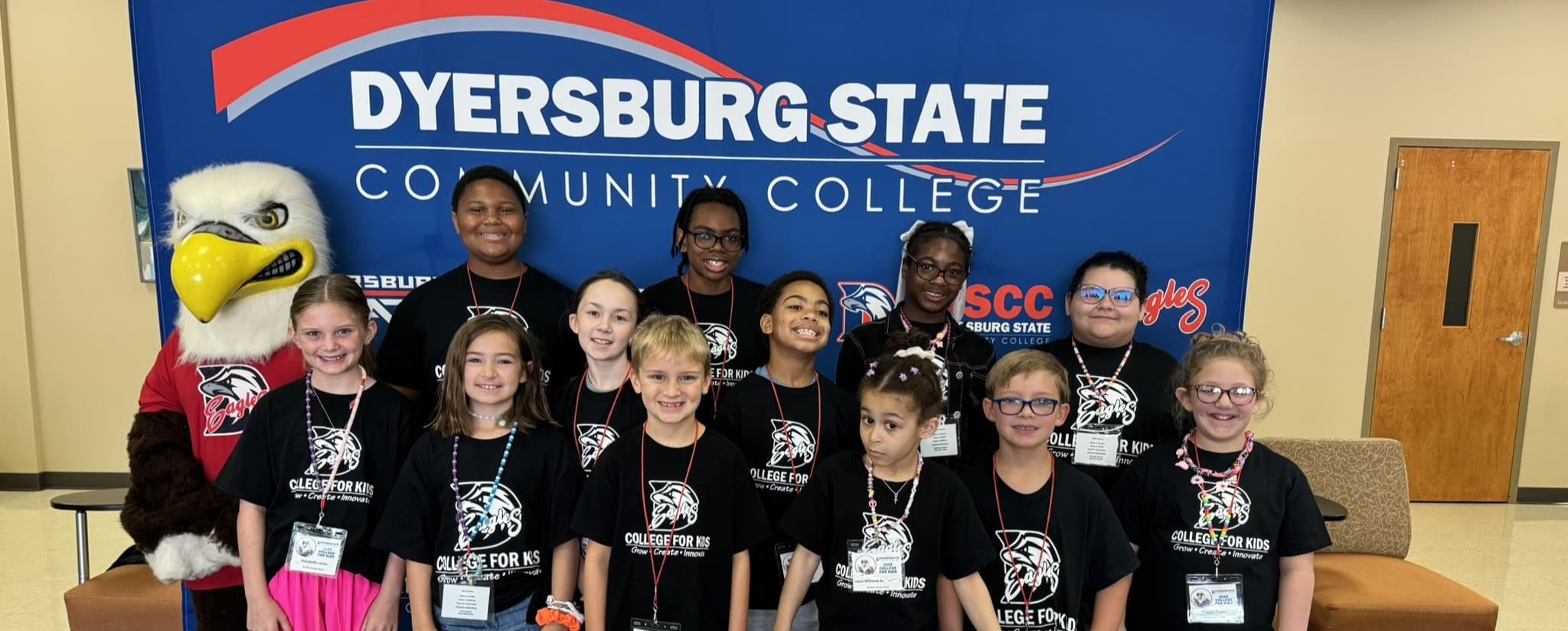 Group of students standing in front of a DSCC backdrop with the Eagle Mascot at the Jimmy Naifeh Center.