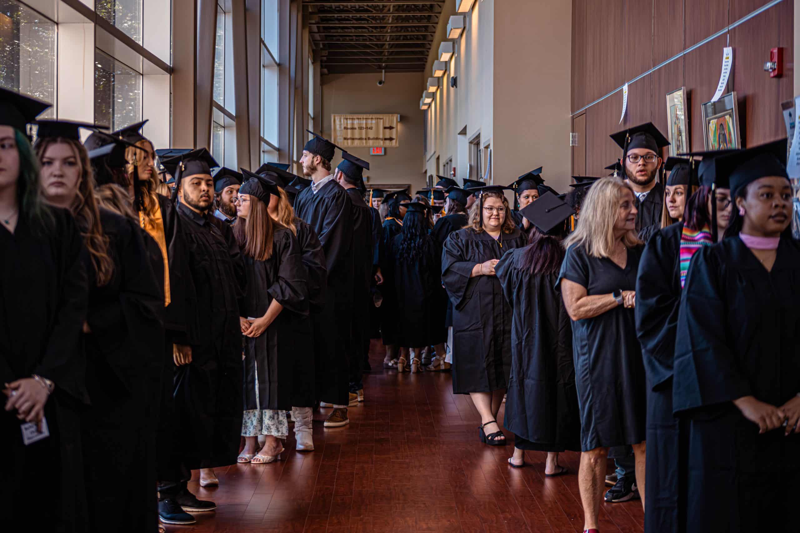 A group of graduating students stands in the LRC hallway, waiting for the processional to begin.