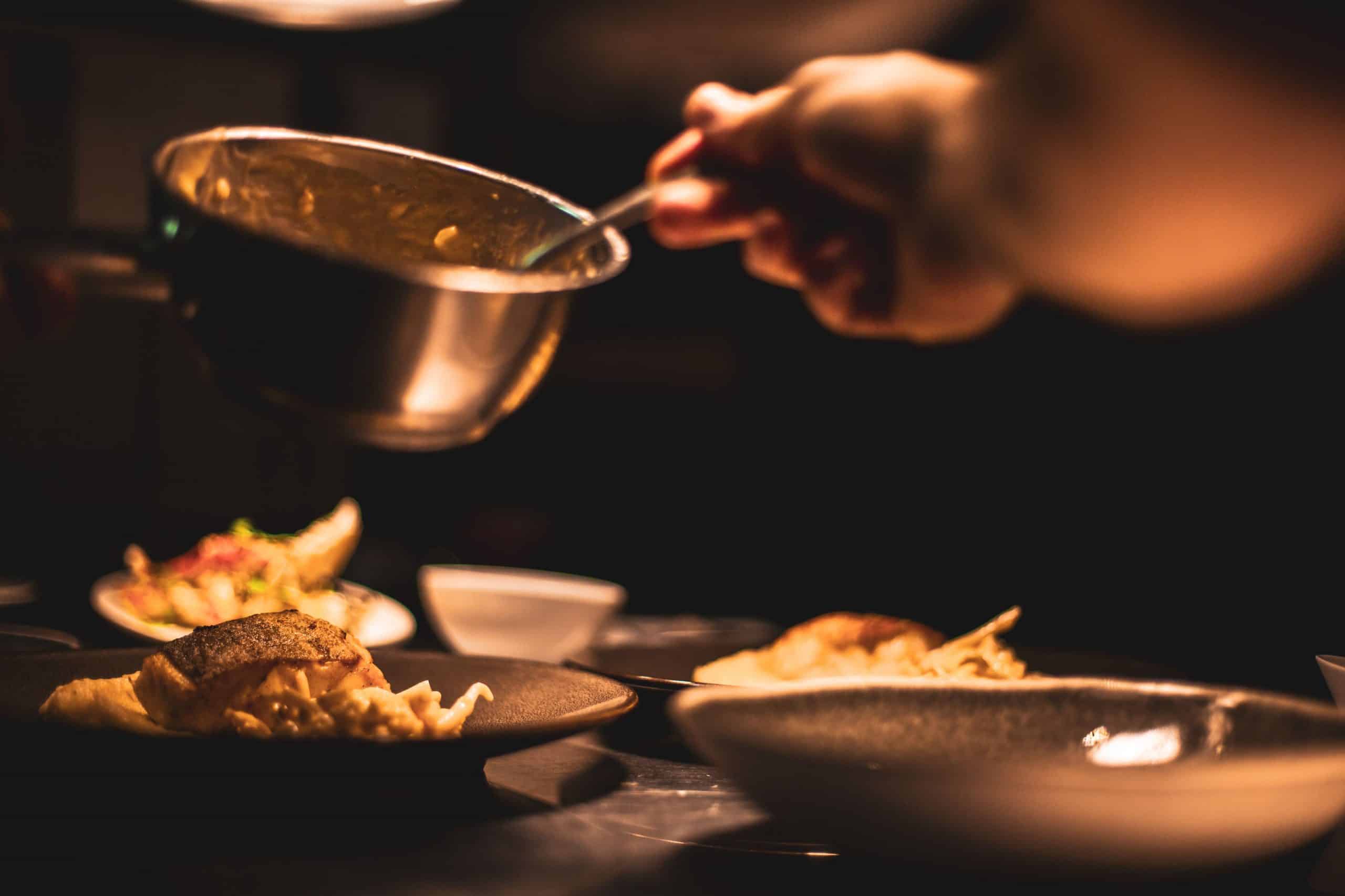 Chef plating a prepared dish in a commercial kitchen, holding a mixing bowl while adding finishing touches to the meal.