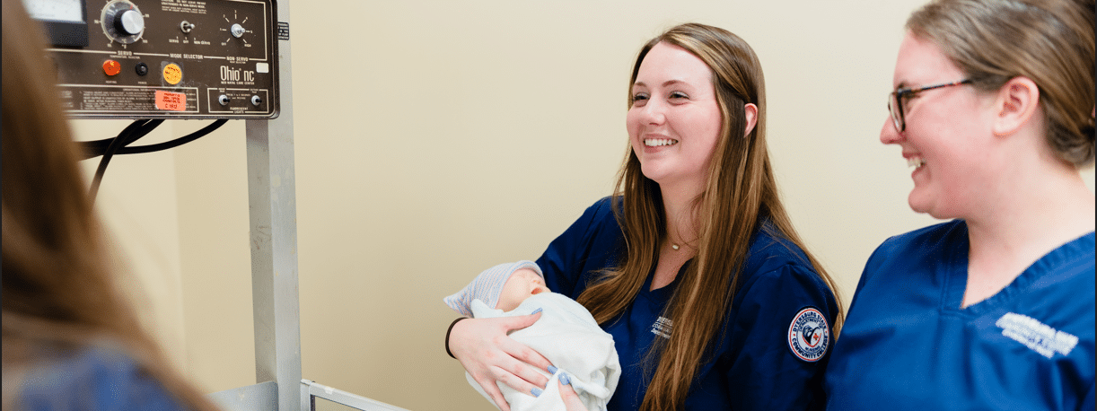 Image of two nurses in a NICU room holding a baby.