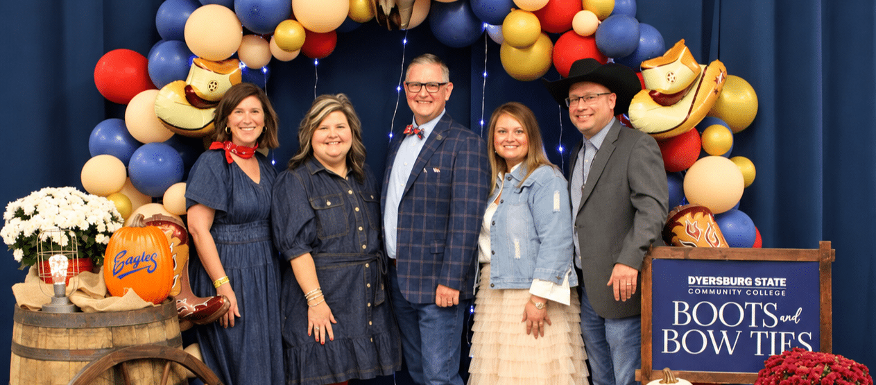 Image of five individuals standing together and smiling with a western-themed background during the Boots & Bow Ties event.